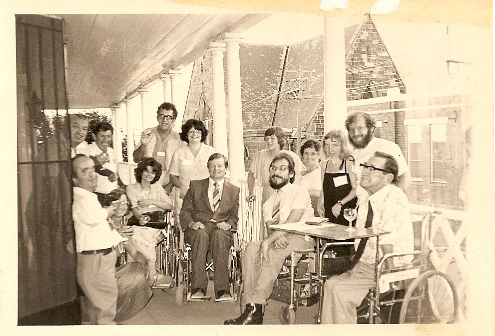A group of people with disability sitting, and standing together. The photo looks old.