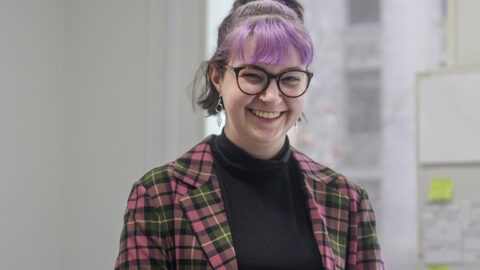[IMAGE Photograph of Issy Hay, a smiling young, white person with a purple fringe, leaf earrings, a nose ring and a plaid blazer.]