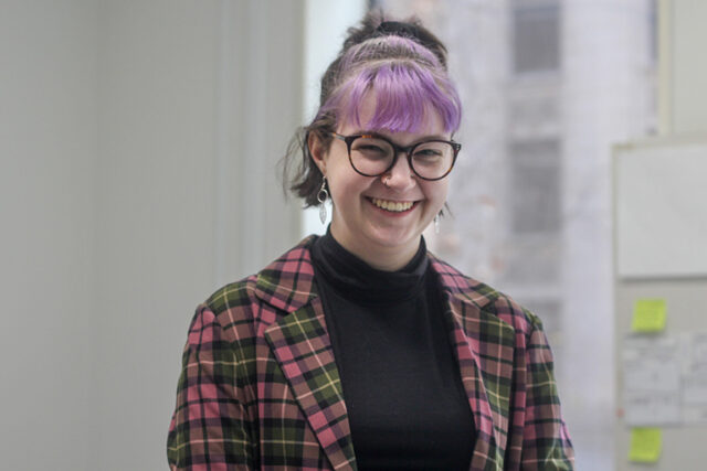 [IMAGE Photograph of Issy Hay, a smiling young, white person with a purple fringe, leaf earrings, a nose ring and a plaid blazer.]