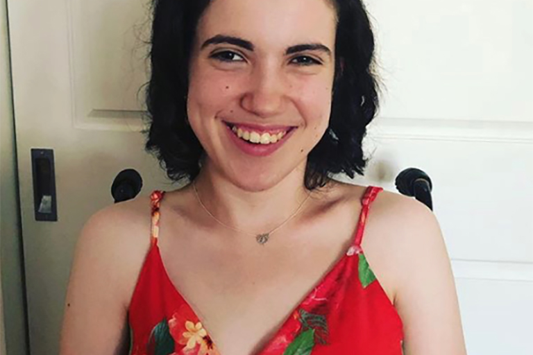 [IMAGE Photograph of Hannah Diviney, a smiling, young white woman with dark hair, wearing a red floral top. The handlebars of her wheelchair are visible behind her shoulders.]
