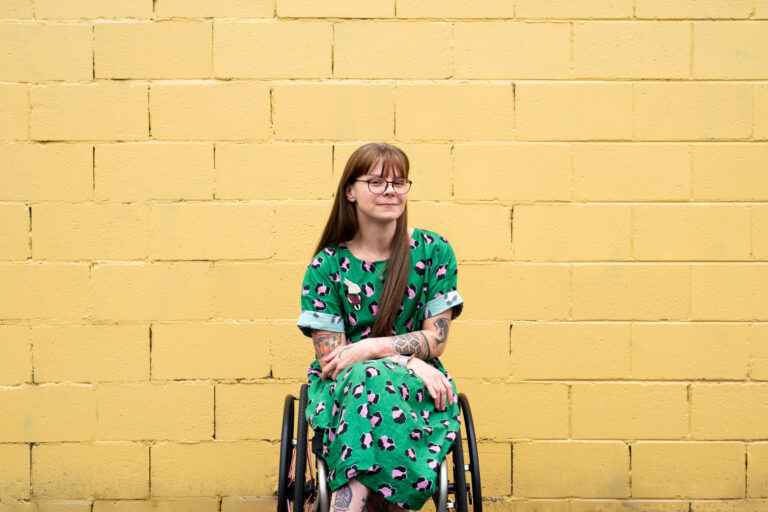 Photo of Nicole Lee wearing a green dress against a yellow brick background
