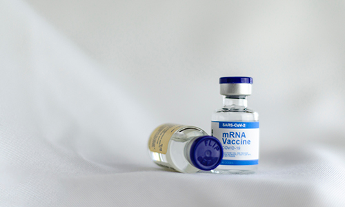 Two vials on a white surface, one labelled MRNA vaccine.