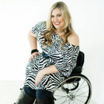 Marayke Jonkers is smiling, has long blonde wavy hair and is wearing a black and white zebra pattern dress with black boots and is in a wheelchair.