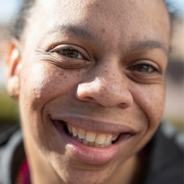 Close up of the face of a woman smiling happily at the camera, sunlight is illuminating part of her face.