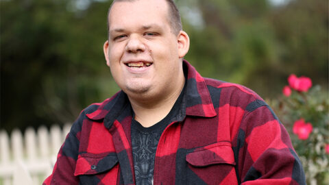 a man wearing a black and red checkered shirt smiles at the camera