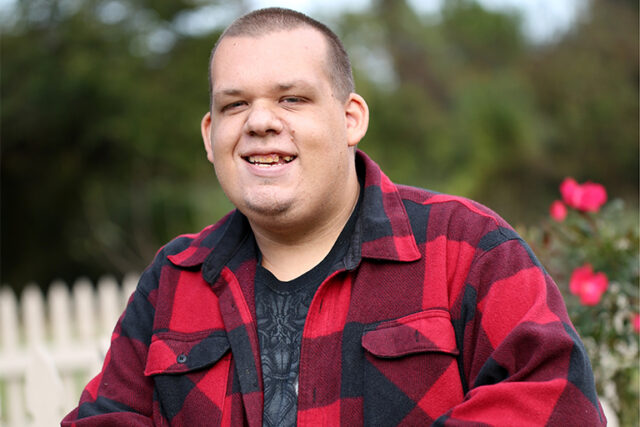 a man wearing a black and red checkered shirt smiles at the camera