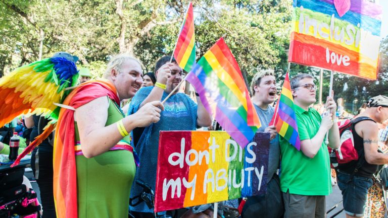 People at Mardi Gras wearing rainbows with a sign that reads 'don't dis my ability'.