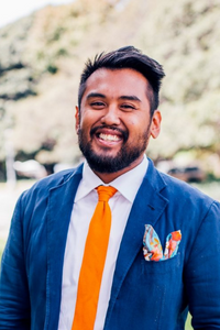 Giancarlo De Vera smiling outdoors wearing a blue sit and orange tie