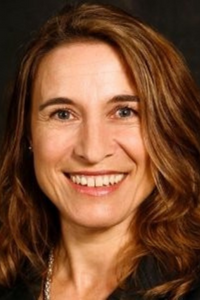 Photo of Karin Waldmann smiling at the camera. She has shoulder-length brown hair.