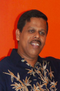 Photo of Sunil Fernando smiling in front of a bright orange background