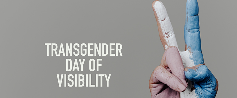 [A hand displaying the LOVE sign in Auslan in blue, pink and white is positioned next to the words Transgender Day of Visibility]