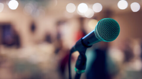 [IMAGE a microphone is in focus in the foreground against a blurry background]