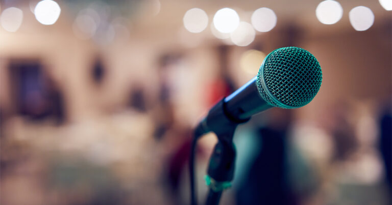 [IMAGE a microphone is in focus in the foreground against a blurry background]