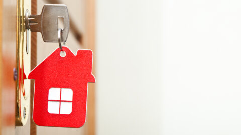A key ring in the shape of a red house attached to a key in a door