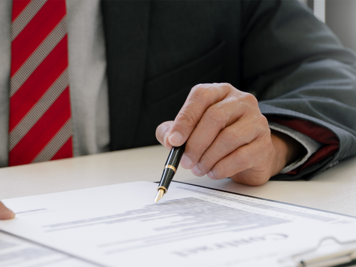 Image of a person sitting a desk wearing a suit and tie, writing on a document