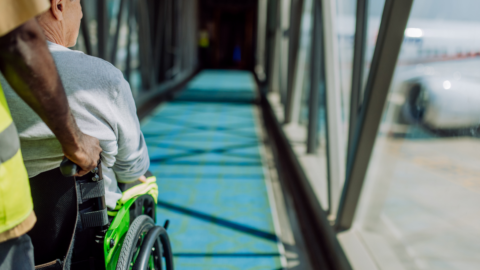 A person is being pushed in a wheelchair down an airport concourse