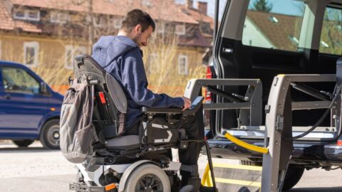 A person is being lifted into an accessible taxi in their wheelchair