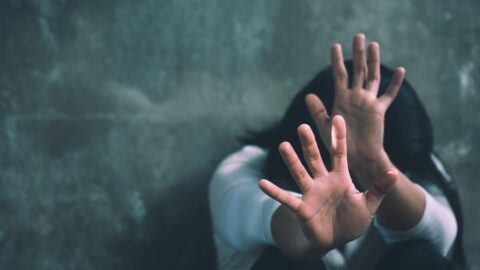 A person is sitting against a wall with their hands out defensively protecting themselves