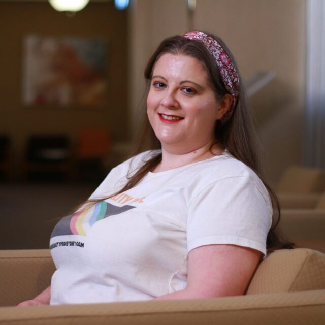 Image of Hannah Solomons wearing a white t-shirt with disability pride flag