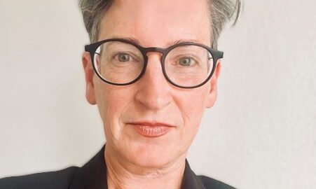 Image of Naomi Anderson wearing a black blazer and black framed glasses