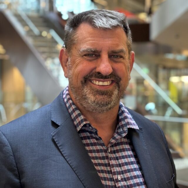 Prof Scott Avery headshot wearing a blue check shirt and a blue blazer