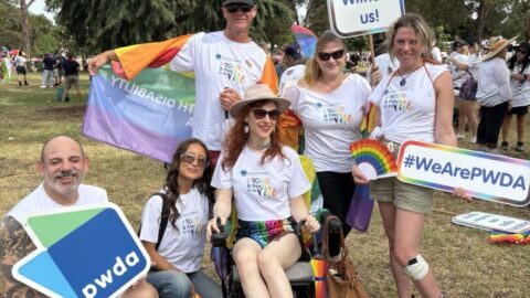 A group of people dressed and ready for the Midsumma Pride March. They are holding signs and wearing rainbow capes.