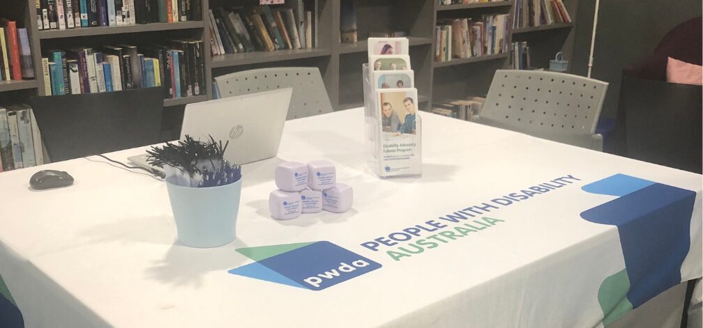 A desk set up at an event with banners and PWDA collateral