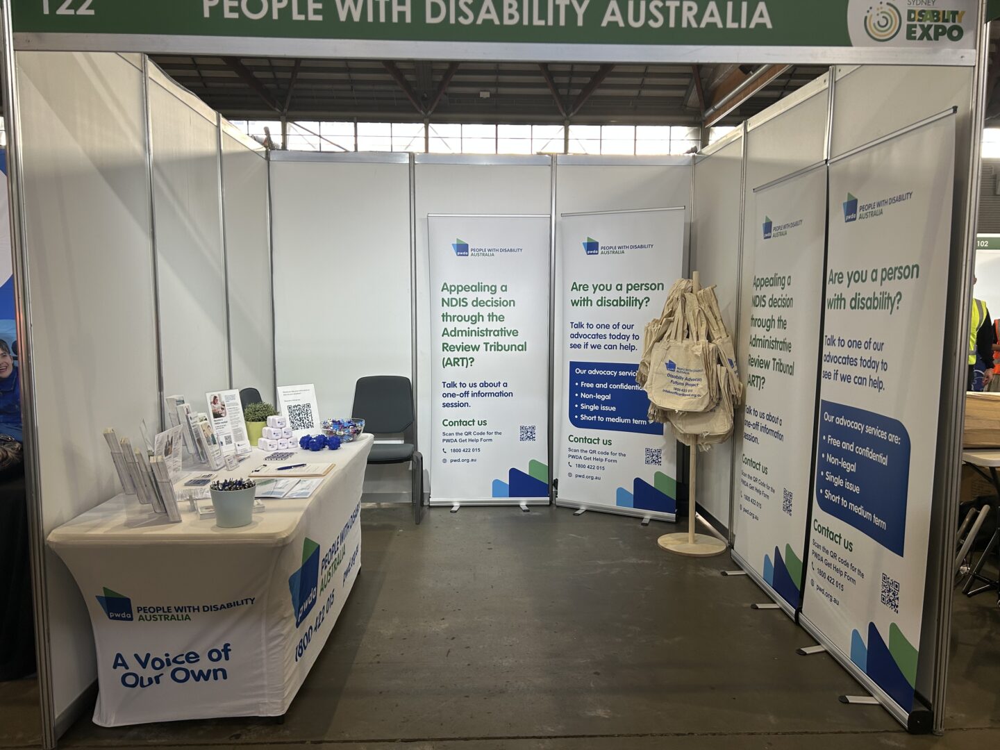 Exhibition booth for People with Disability Australia with banners and a table of brochures at a disability expo hall