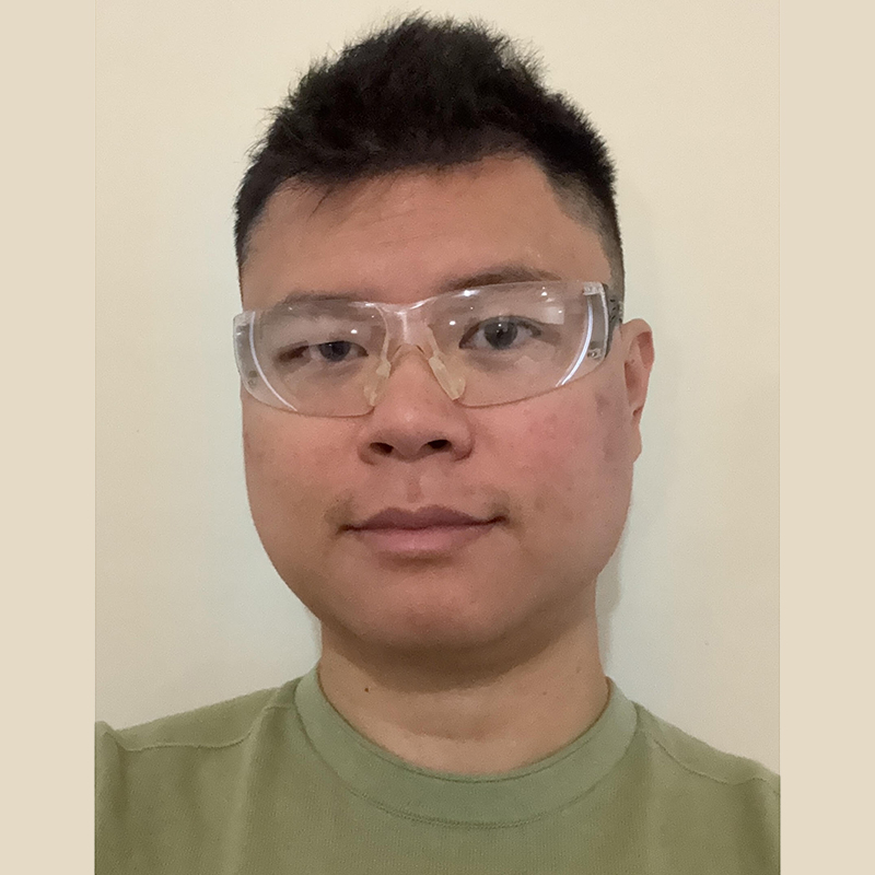 Portrait of a man wearing clear safety goggles and a green shirt, facing the camera.