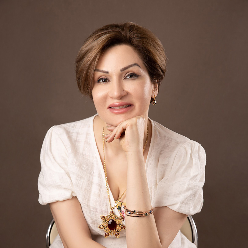 Portrait of a woman with short brown hair in a white blouse, resting her chin on her hand.